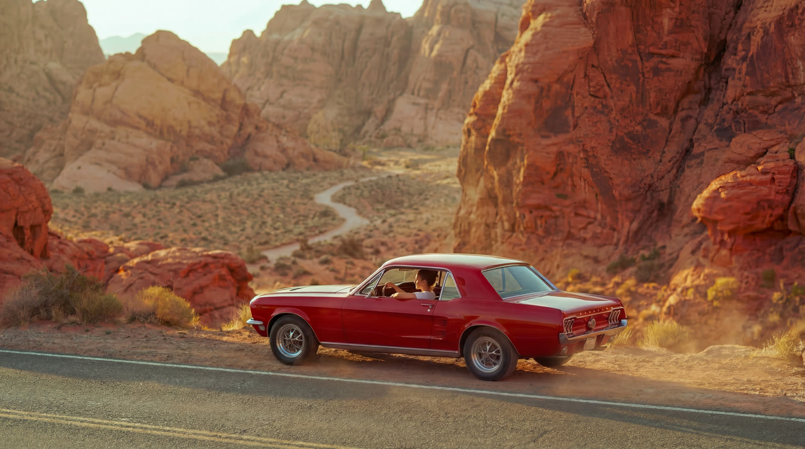 The car small on the road, surrounded by red rock